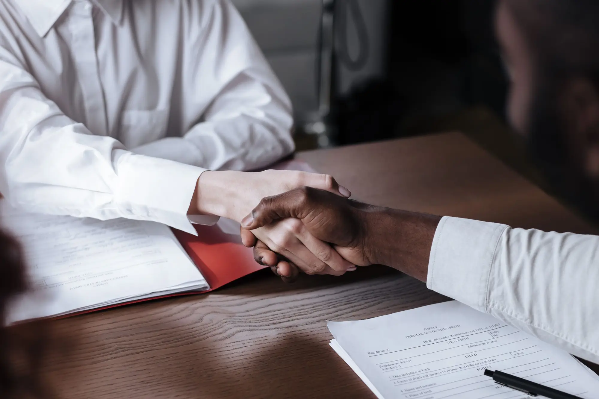 Two people shaking hands over documents on a table